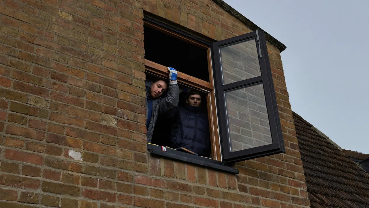 Two fitters carefully removing an old window frame from a brick house